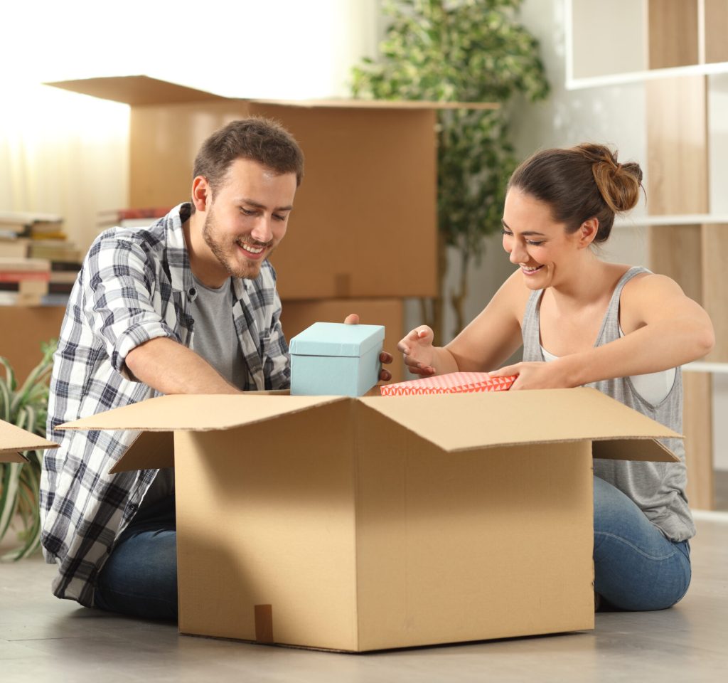 Happy couple unboxing belongings moving home sitting on the floor